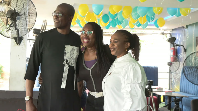 Three members posing together under green and yellow balloons