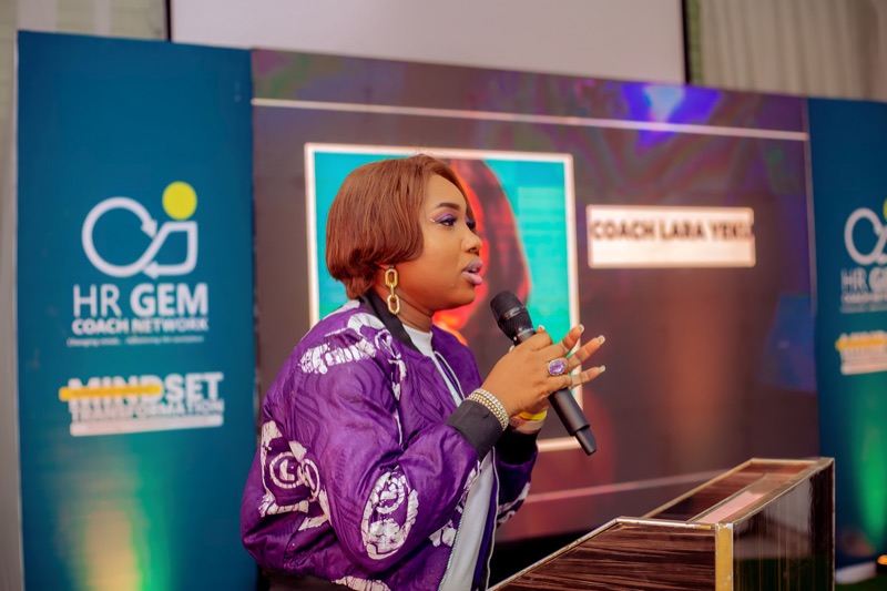 Coach Lara Yeku speaking into a microphone on stage