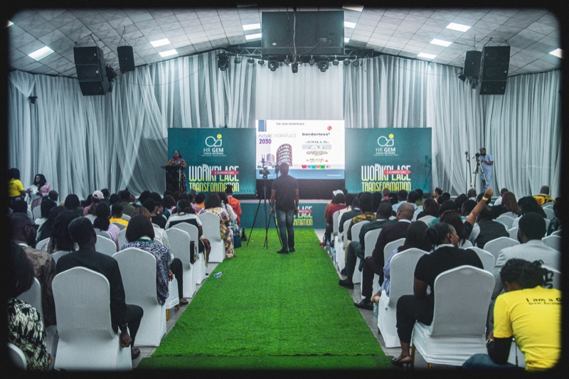 A wide view of the hall, rows of seated guests facing the stage along a green carpet